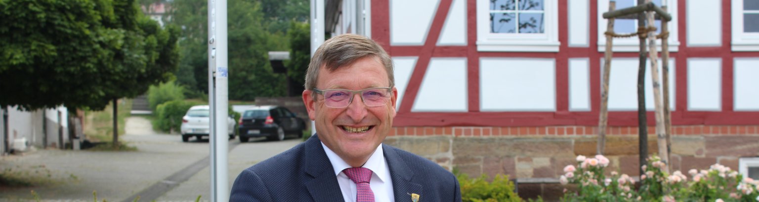 Bürgermeister Frank Grunewald mit Tablet in der Hand auf Bank vor Rathaus sitzend