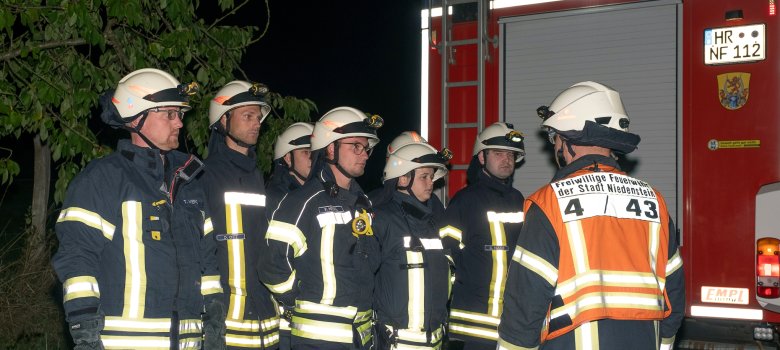 Einsatzbereite Feuerwehrleute stehen in zwei Reihen und werden über den Einsatz informiert