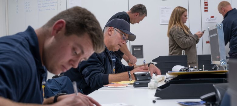 Die Mitglieder der Technischen Einsatzleitung sitzen am Tisch und bearbeiten Einsatzmeldungen